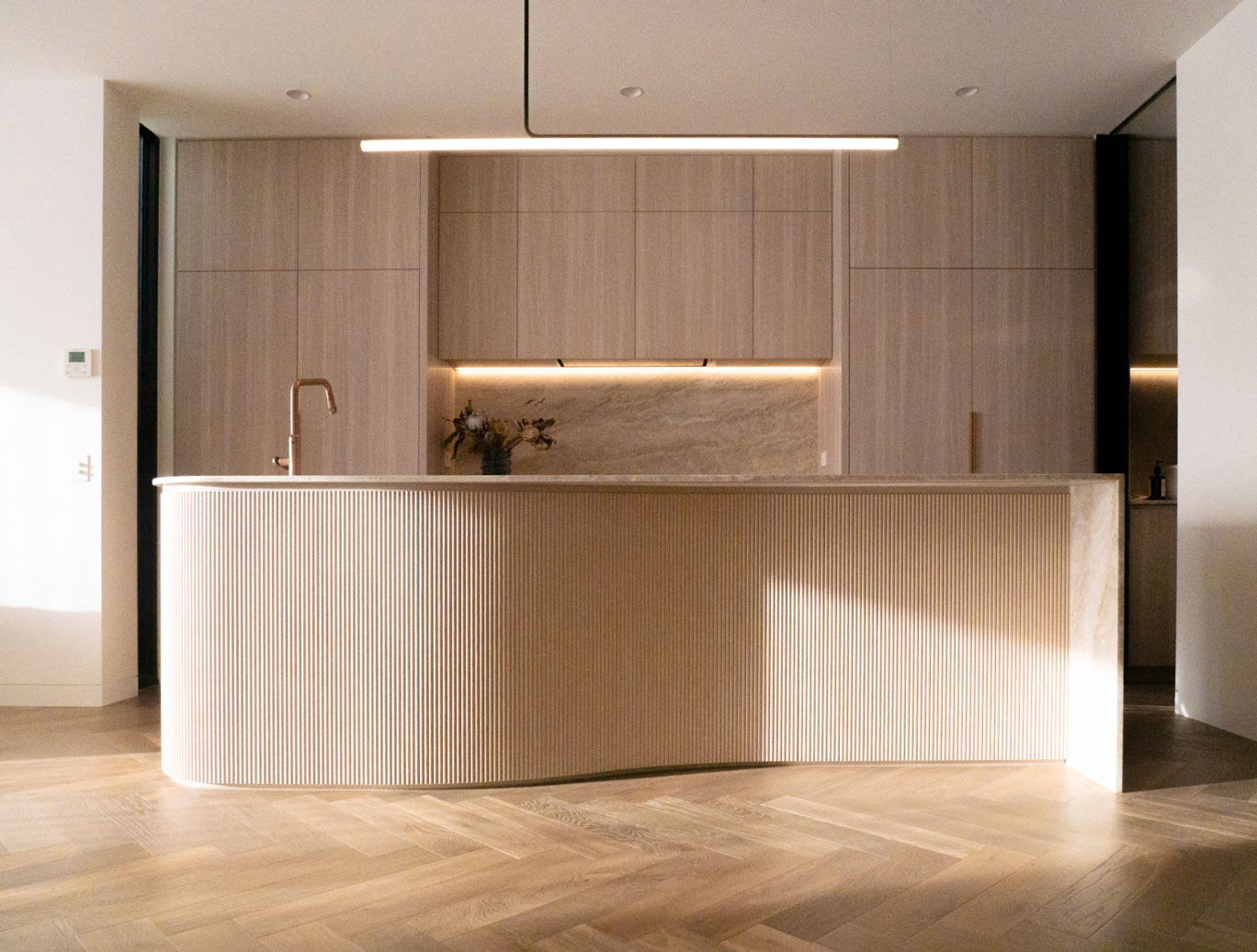 Russell Lea Residence kitchen — interior design by Mike & Morlly Architects Russell Lea Residence minimalist kitchen with curved fluted island, travertine benchtop, oak joinery and herringbone timber floor — interior design Sydney by Mike & Morlly Architects