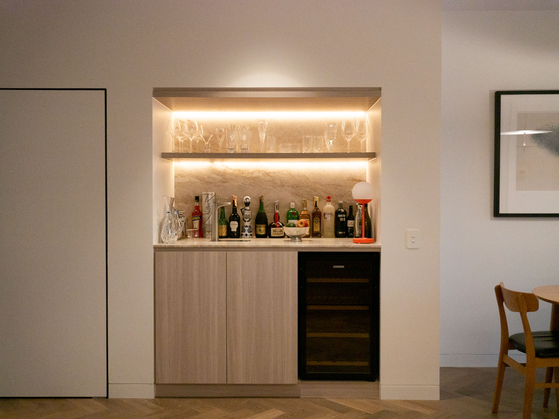 Integrated bar recess with backlit shelving and stone backdrop at Clara Residence