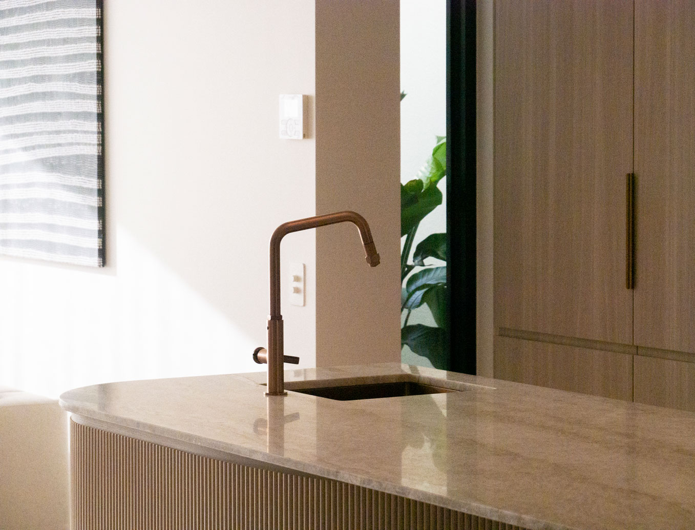 Sculpted curved kitchen island with fluted timber and copper tapware at Clara Residence