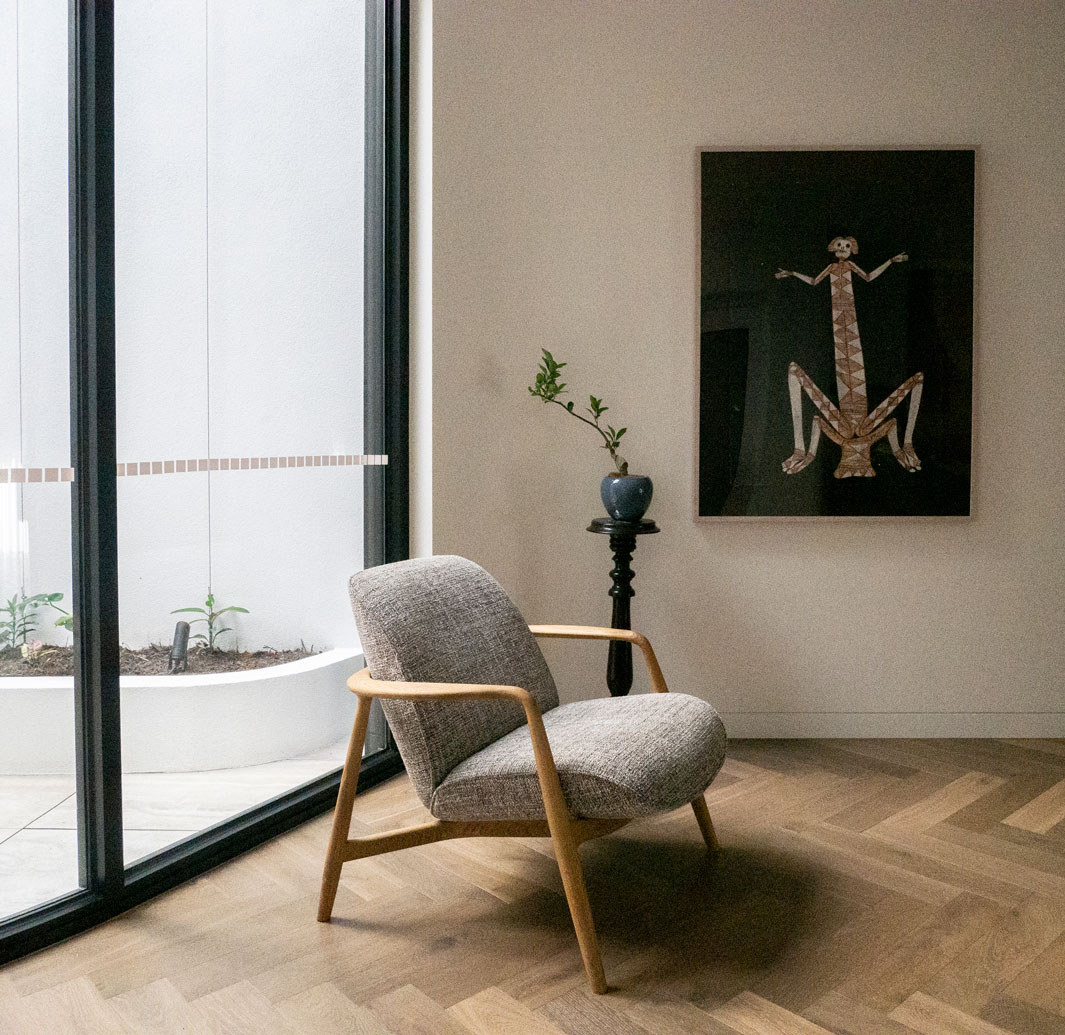 Gallery-like entry with sculptural chair, framed artwork, and herringbone timber flooring at Clara Residence