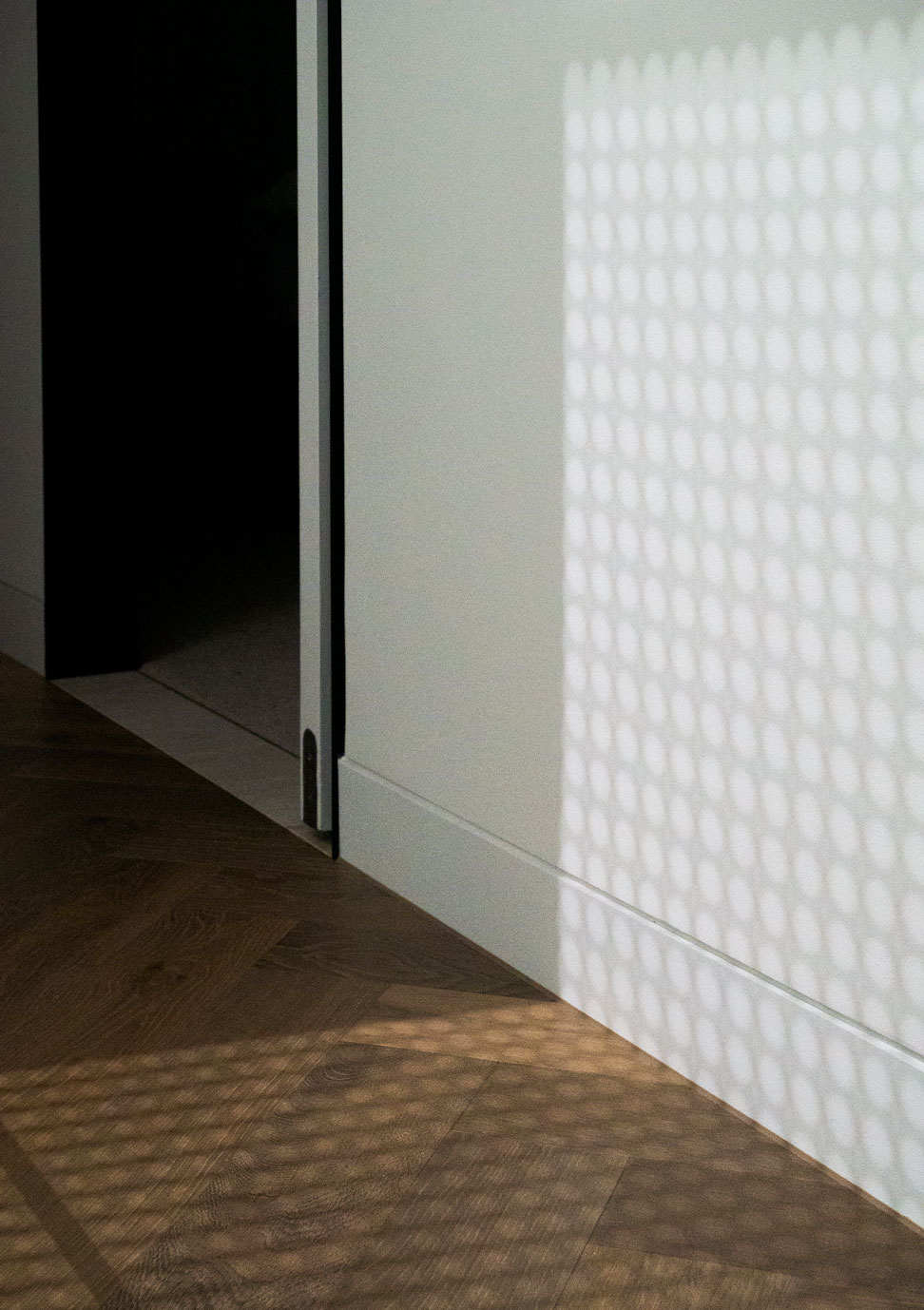 Patterned light from perforated screen falling across timber flooring at Clara Residence