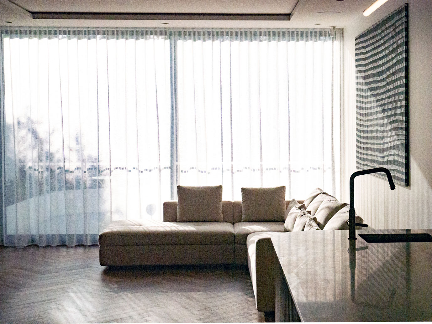Living area with sheer curtains, soft sectional, and stone island bench at Clara Residence