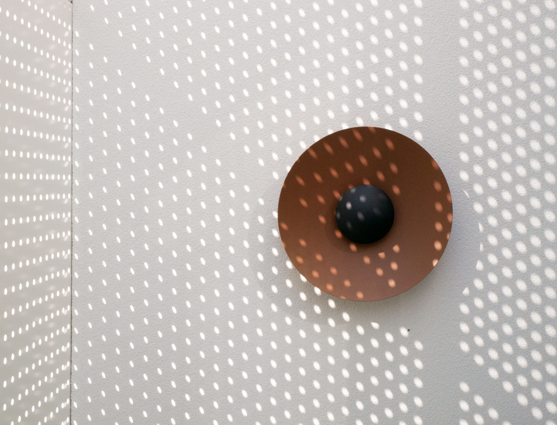 Copper sconce against a perforated screen casting dotted light at Clara Residence