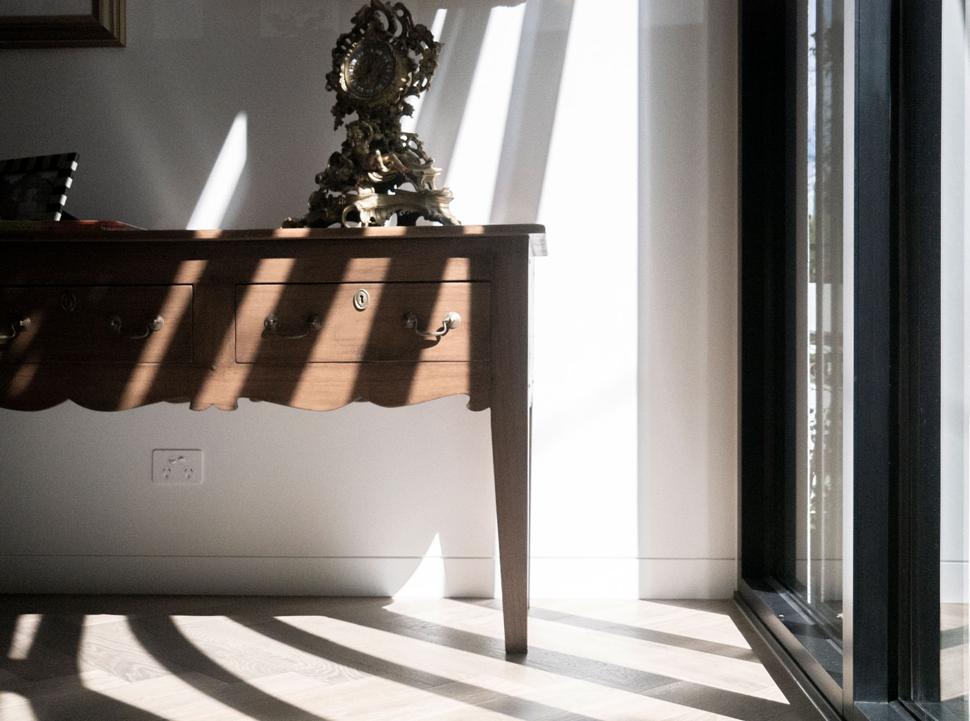 Soft shadow lines cast across an antique timber console at Clara Residence